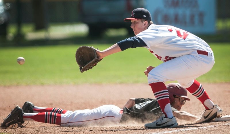 PICK PLAY &#8211; First baseman Blake Morris of the St. Albert Cardinals is on the receiving end of a pick off attempt as the Okotoks Dawgs Black base runner is safe sliding