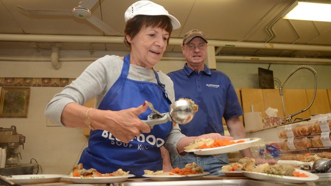 Rose Wasyluk, a nine-year veteran volunteer at the Blue Door Soup Kitchen, serves up Thanksgiving meals on Friday as soup kitchen manager Bill Hickey looks on. (Arron Pickard/Sudbury.com)