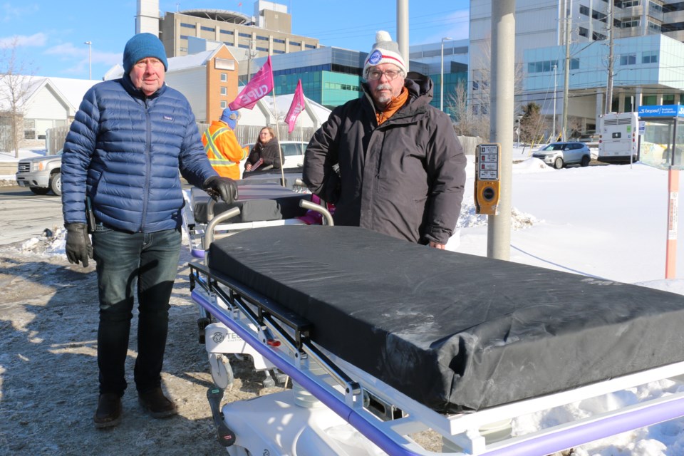 Michael Hurley, president of the Ontario Council of Hospital Unions/CUPE at left with CUPE researcher Doug Allan standing outside Health Sciences North in Sudbury with hospital stretchers.