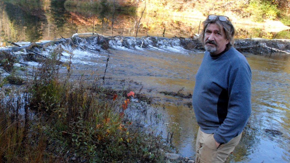 Ralf Albrecht stands next to a beaver dam that accompanies a boom on Windy Creek downstream of his house, where much of the boom can be found underwater.