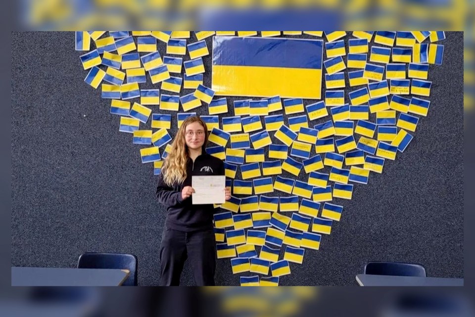 Rochelle Lavrivière stands in front of a heart-shaped display of small Ukrainian flags at École secondaire du Sacré-Coeur. Students wrote messages of hope and solidarity with the Ukrainian people on the flags.