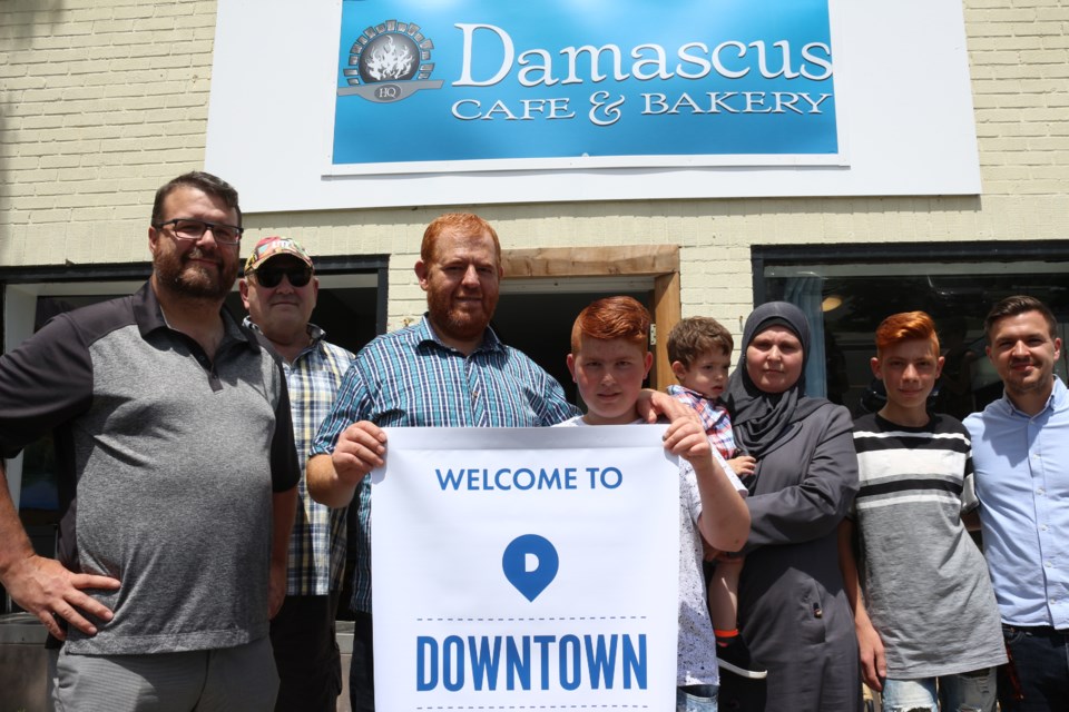 The Qarquoz family, owners of Damascus Cafe and Bakery on Beech Street, show off a banner welcoming them to the downtown. Downtown BIA chair Jeff MacIntyre, left, and Peddlers Pub owner Dennis Gainer, second from left, as well as Nico Taus, from Studio123, right, were on hand to present the family with a donation to help them recover from recent vandalism. (Arron Pickard/Sudbury.com)