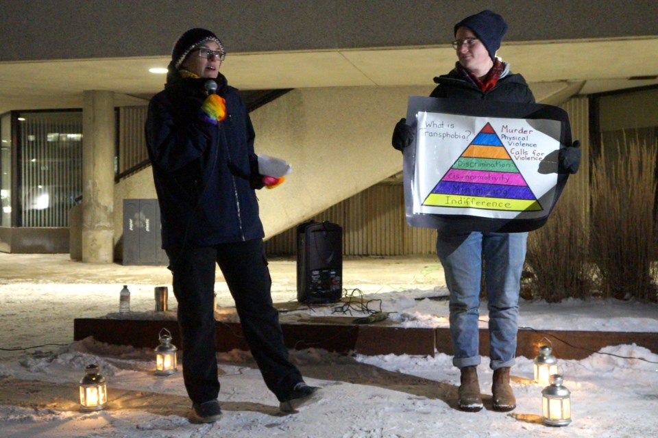 Laur O’Gorman, a former Gender Studies professor at Laurentian University, offers information on the many types of harms transphobia can cause. Aspen Groom holds the poster showing, at the bottom level, indifference, and at the top, murder. 