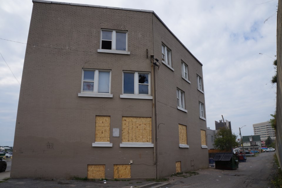 The back of the building that runs from 352 Elgin Street to 362 Elgin Street. Several windows have been boarded up and others are broken. Just down the alley is Greater Sudbury Fire Services and the Multicultural and Folk Arts Centre can be seen in the far right. 