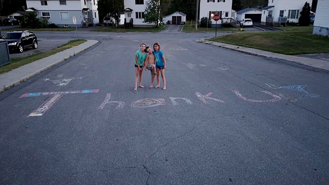 Although only three of them appear in the photo, Braedon Roney, Avery Roney, Kolby Dusik, Jayden Dusick and Hannah Brooks are so grateful for the work Ontario FireRangers and water bombers are doing to battle the dozens of forest fires burning across the northeast that they drew an enormous chalk “Thank You” message on their street for the pilots to see. (Supplied)

