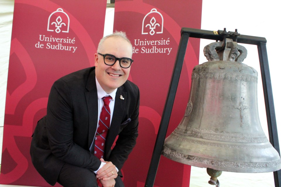 Université de Sudbury president Serge Miville poses Sept. 25, 2024 with the historic bell that goes back to the school’s roots more than 100 years ago. The bell has been used as the basis for U of S’s new brand identity, as seen on the banners behind him.