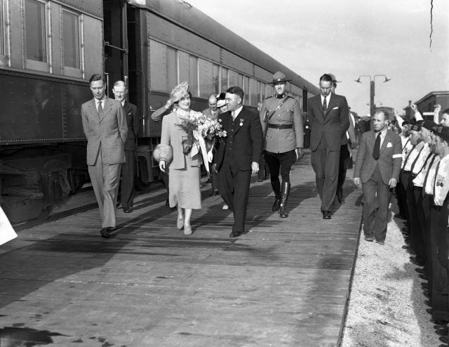 King George VI and Queen Elizabeth walking beside their train with Capreol Mayor James E. Coyne, various dignitaries and Mounties in Capreol. A crowd is gathered to greet them including military personal. (Sudbury Star Fonds, City of Greater Sudbury Archives)