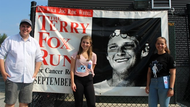 Terry Fox Run 2017 organizers Ben Mackenzie, left, Ashley Lavigne and Melanie Rose Frappier pose in front of a picture of Terry Fox on Sunday at the Bell Park Amphitheatre. (Darren MacDonald)
