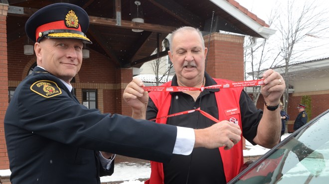 In this 2016 file photo, Greater Sudbury Police Chief Paul Pedersen and Action Sudbury chair Ron Roy tie red ribbons to a car after the launch of the 28th annual Red Ribbon campaign in Greater Sudbury. (File)
