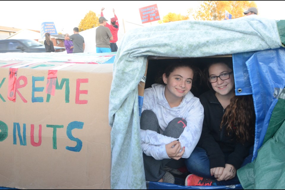 Grade 9 students Kaylee Leclair and Mackenzie Roy peek out through the box that would serve as their sleeping quarters for the night, as other students in the background hold signs to raise awareness of homelessness. (Arron Pickard/Sudbury.com)