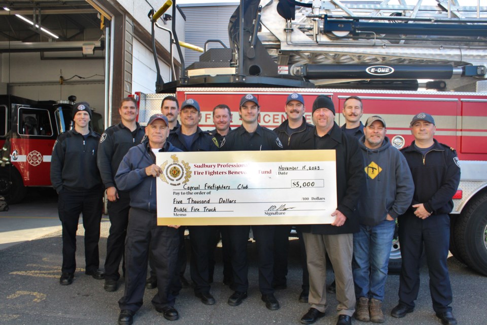 Capreol emergency services station Capt. Scott Robinson and Sudbury Professional Fire Fighters Association and Capt. Mike Squarzolo hold up a novelty cheque, joined by career firefighters at the downtown station earlier this week. 