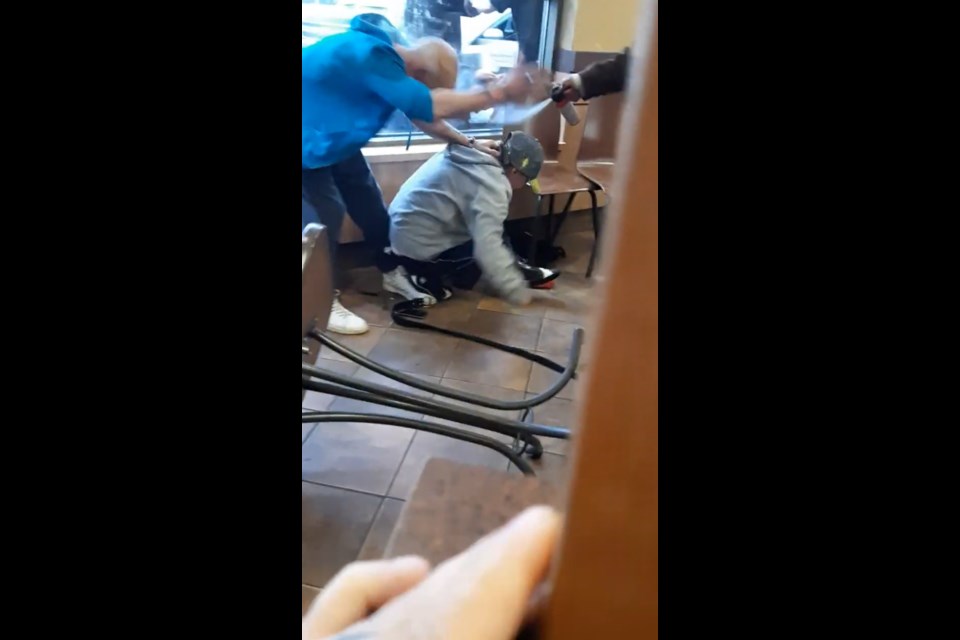 As the knife-wielding man holds a woman by the neck on her knees, video from another Tim Hortons customer captures the moment bear spray was used to try to stop him. (Screen capture)