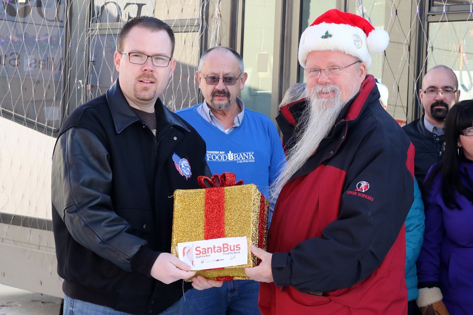 Amalgamated Transit Union Local 966 president Ken Koza (left) presents a present to Thunder Bay Food Bank chair Reino Pitkanen on Monday, Dec. 12, 2016 (Leith Dunick, tbnewswatch.com). 