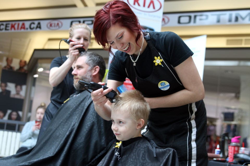 Hairstylists Rene Rypkema (left) and Amanda Puukila (right) at Carlo & G Hair and Esthetics shave the heads of Thunder Bay Police Service const. Matt Sombrutski and his three-year-old son, Oliver during Cops for Cancer. 