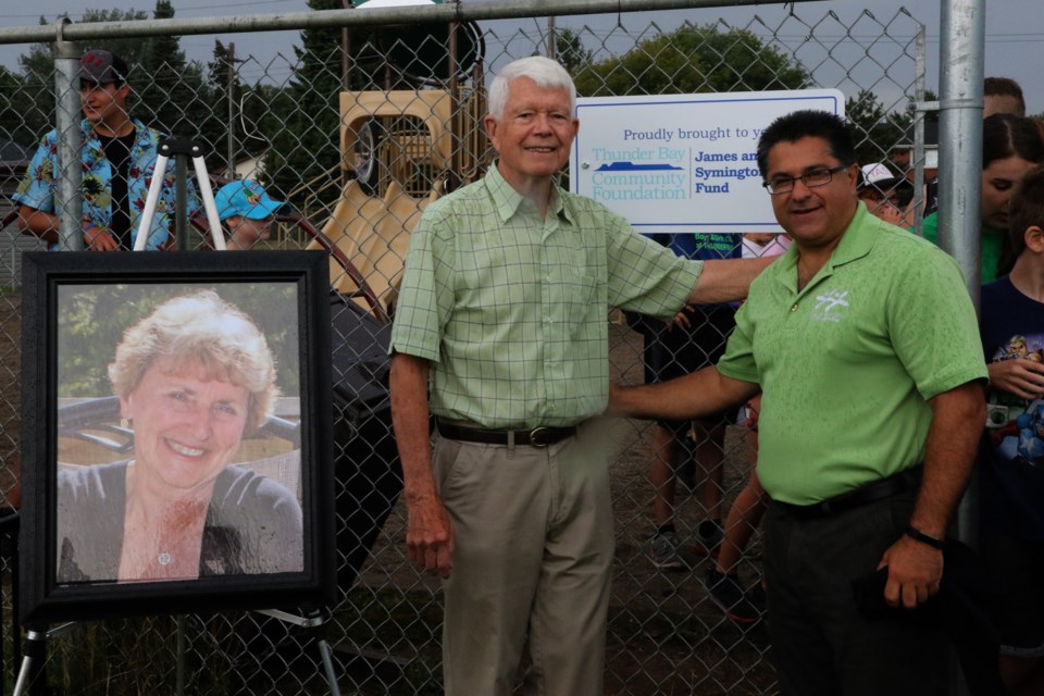 Jim Symington (left) and executive director Albert Aiello stand next to a portrait of the late Shirley Symington at the unveiling of the Boys and Girls Club play structure. (Michael Charlebois, tbnewswatch)