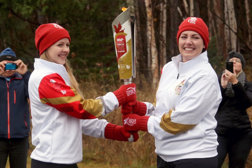 Acting Mayor Shelby Ch'ng (right) passes off the Canada Games Torch to synchronized swimmer Brianna Johnson on Thursday, Oct. 25, 2018 outside Lakehead University. (Leith Dunick, tbnewswatch.com)