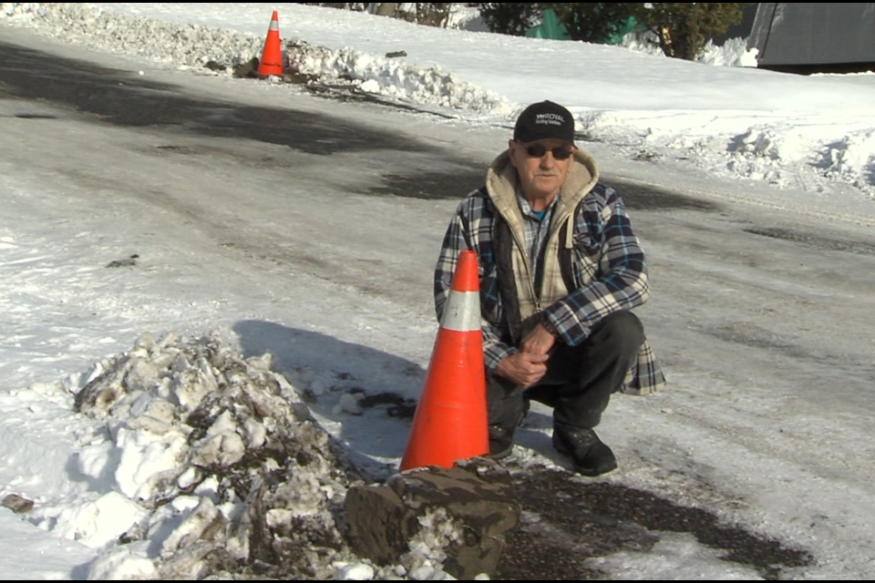 Don Williams crouches beside one of the curbstones dug up by a grader clearing his street (Jon Wilson/TBTV photo)