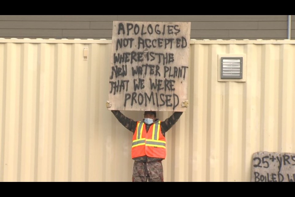 A Neskantaga resident holds a sign protesting the ongoing lack of safe drinking water in the First Nation, 400 km north of Thunder Bay (Troy Charles/TBTV photo)