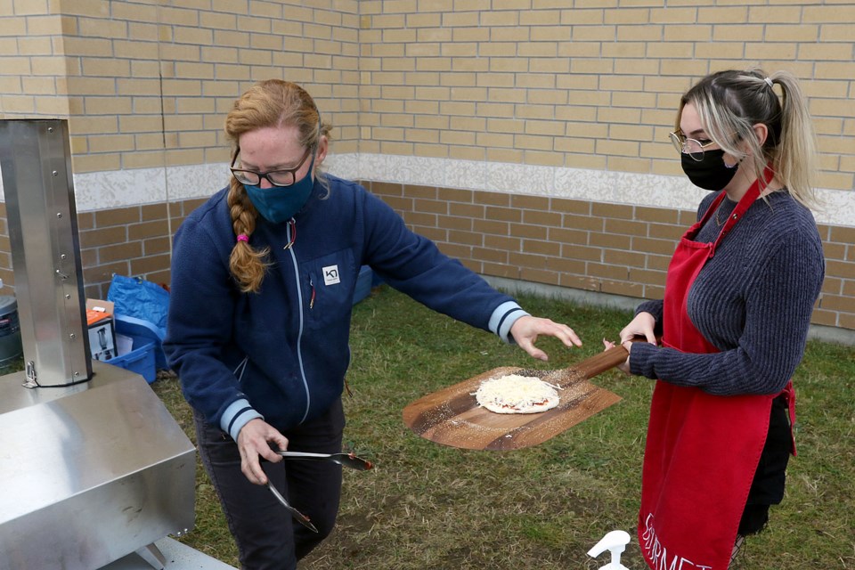 Roots to Harvest's Erin Beagle (left) helps Superior Collegiate student Chayse Holland, 16, cook a pizza over an outdoor pizza oven on Friday, Oct. 9, 2020. (Leith Dunick, tbnewswatch.com)
