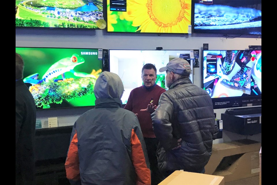 A salesperson shows customers TVs at The Power Centre on Monday. 