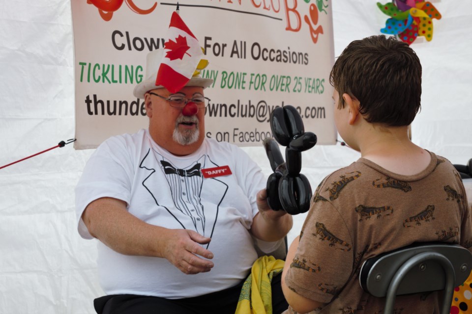 Daffy the Clown, from the Thunder Bay Clown Club, makes balloon animals for children at Thunder Bay's 2023 Canada Day festivities.