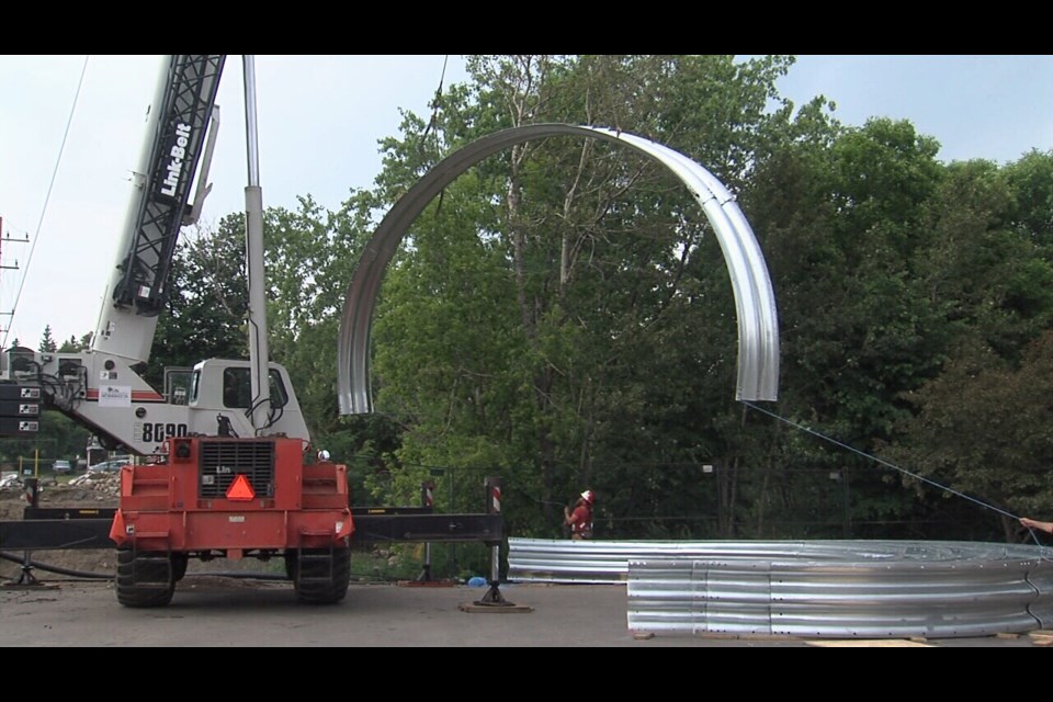 A crane began lifting sections of a steel arch into place over McVicar Creek on River St. on June 28, 2023 (Mike Lang/TBT News)