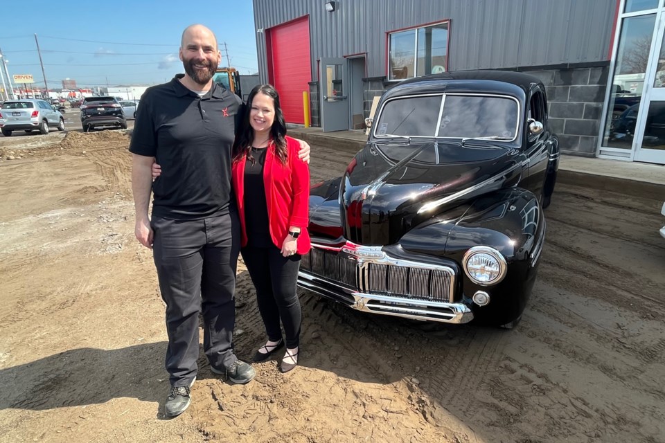 Half-Way Motors' Daniel Trevisanutto (left) and Our Kids Count executive director Jackie Knough pose with a classic car on Thursday, May 11, 2023 outside Car Star Collision's soon-to-open new facility on Carrick Street, announcing this year's Thunder City Rumble. (Leith Dunick, tbnewswatch.com)