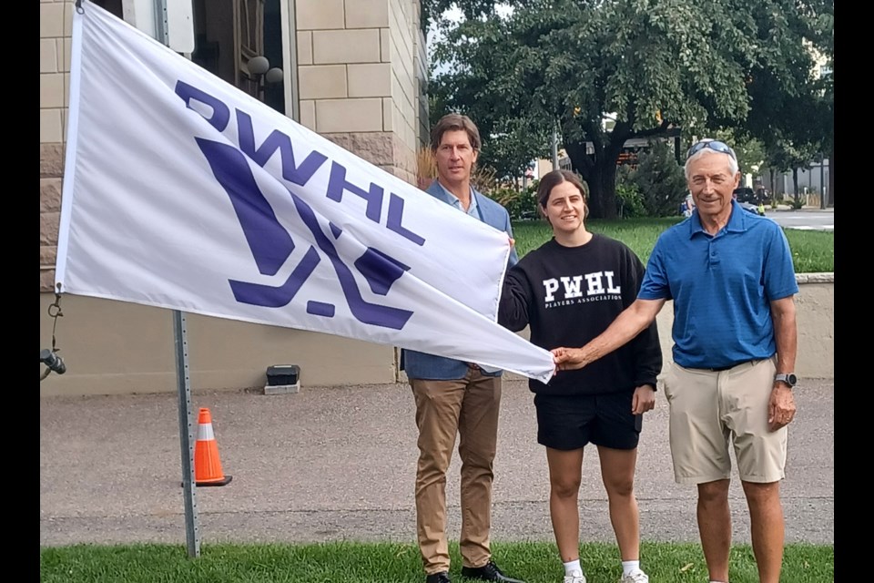 Coun. Greg Johnsen, PWHL star Michela Cava and Northwestern Ontario Sports Hall of Fame president Dave Siciliano pose for a photo with a PWHL flag Aug. 21, 2025, in Thunder Bay.
