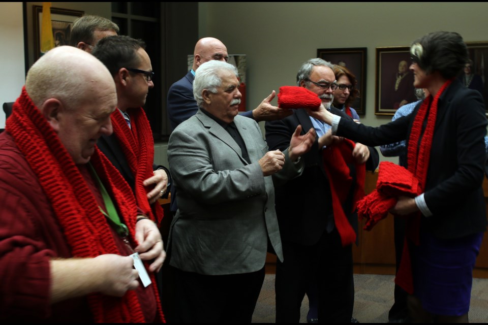 Elevate NWO community developer Tonya Muchano (right) dons city councilors with red scarves on Monday evening to kick off an AIDS awareness campaign leading up to Dec. 1. 