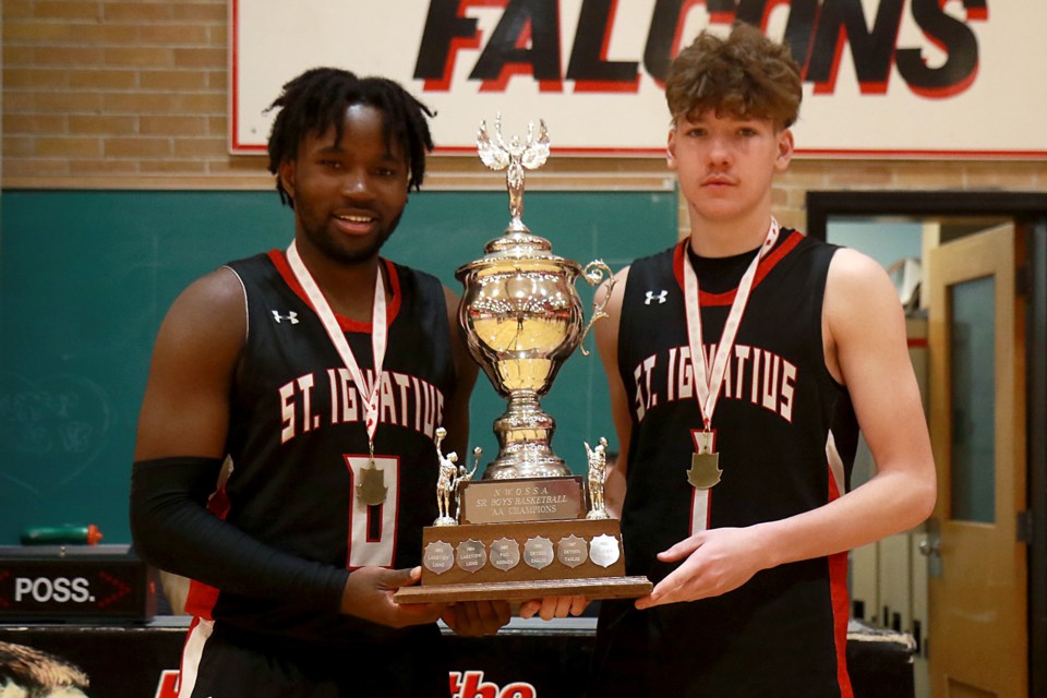 St. Ignatius Falcons captains A.J. Tshilombo (left) and Jackson Lawrence on Saturday, Feb. 25, 2023, accept the NWOSSA 'AA' boys' basketball championship trophy after beating the Beaver Brae Broncos of Kenora 107-34. 