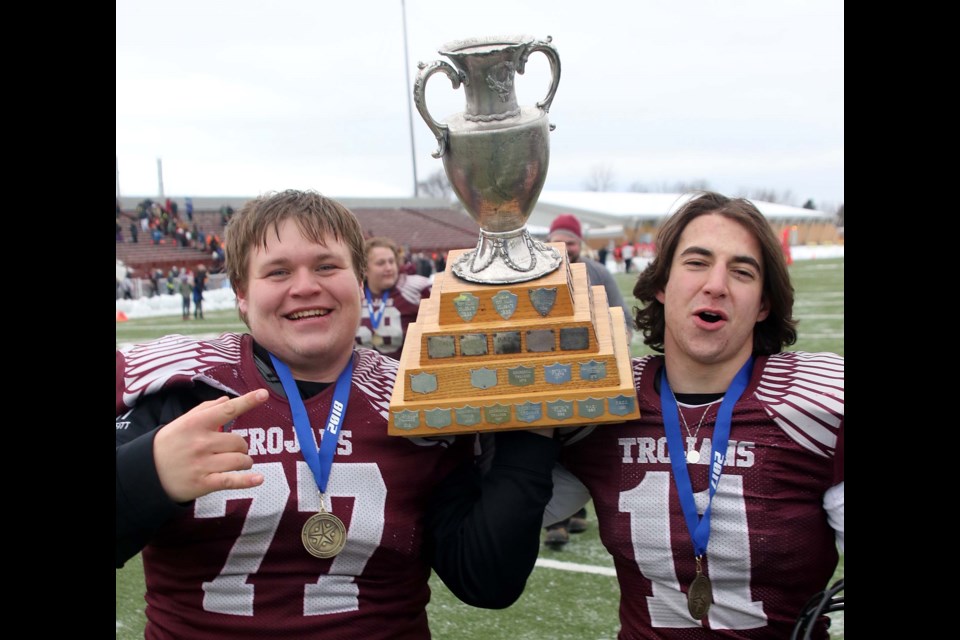 Churchill's Eric Moffitt (left) and Braeden Prochnicki celebrate with the trophy, delivering the Trojan's first senior high school football title since 2012. (Leith Dunick, tbnewswatch.com)