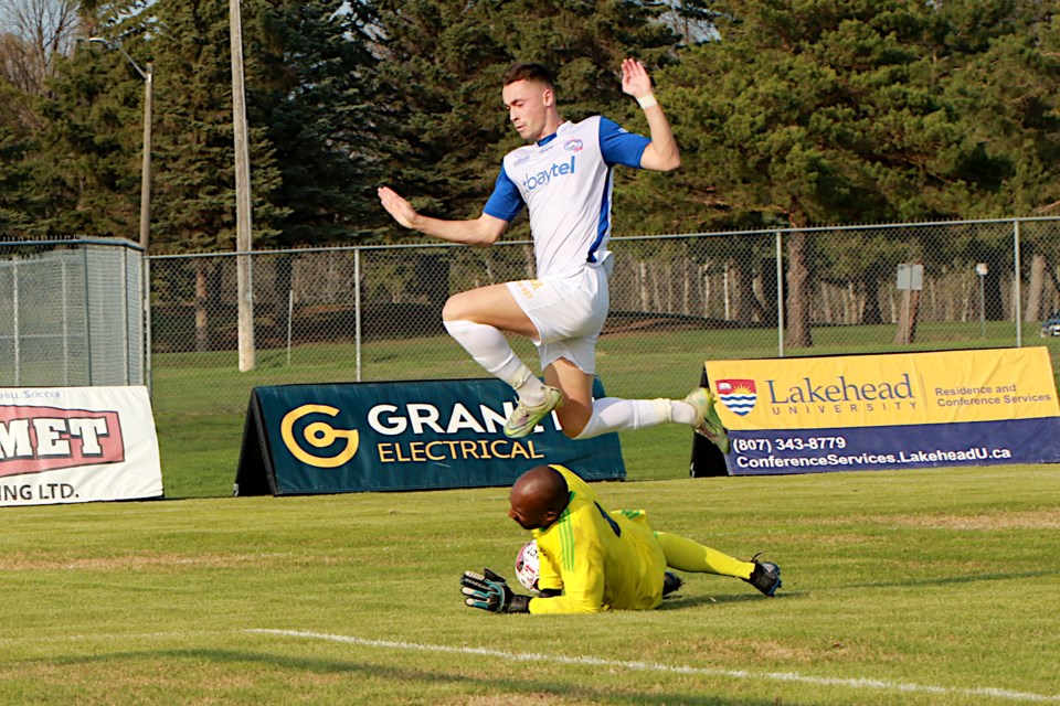 The Chill's Jamie Wynne leapfrogs Winnipeg Lions goalkeeper Jean Michel Ngenzi on Saturday, May 20, 2023 at Chapples Field. (Leith Dunick, tbnewswatch.com)