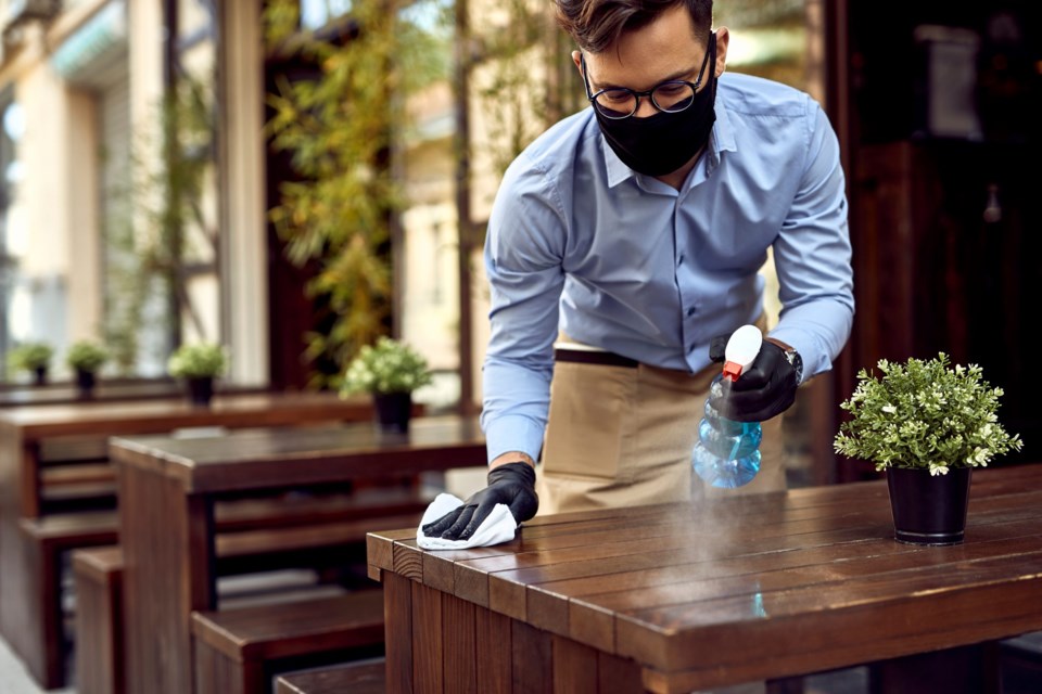 Waiter,Wearing,Protective,Face,Mask,While,Disinfecting,Tables,At,Outdoor