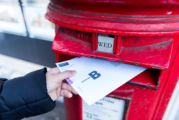 hand putting mail in ballot into a mailbox