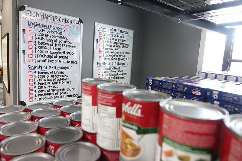 Cans of soup and boxes of pasta line shelves in front of charts showing what goes into food packages from Manitoba Keewatinowi Okimakanak’s new food bank in Thompson, depending on the size of the recipient’s family.