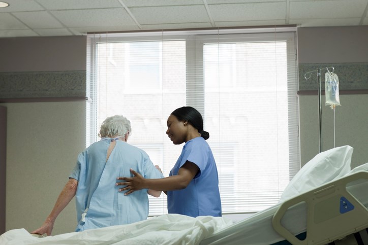 nurse helping elderly patient stand up from bed