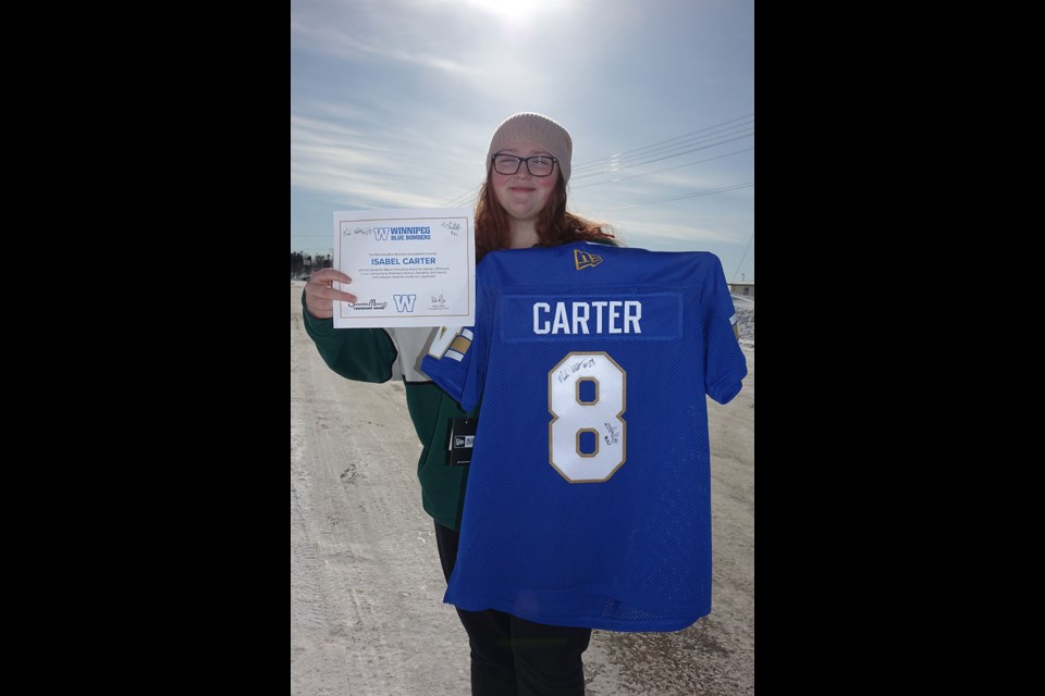 Isabel Carter poses March 21 with her Samatha Mason Friendship Award certificate and her personalized Winnipeg Blue Bombers jersey signed by Nick and Noah Hallett.