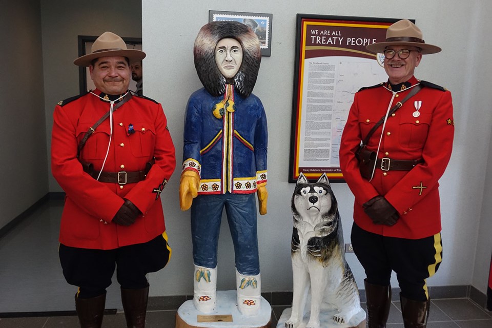 Indigenous Special Constables Ryan Wrightson, left, and Rob Cleveland, right, pose with a wood carving honouring the contributions of Indigenous special constables in the Thompson RCMP detachment lobby.