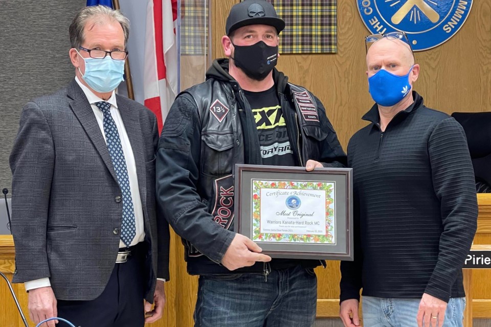 Warriors Motorcycle Club receives its award for having the most original entry in the 2021 Timmins Santa Claus Parade. The award was handed out by Timmins Mayor George Pirie, left, and BIA president Jamie Roach, right.