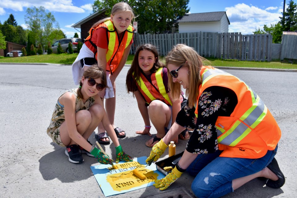 Crystal Percival of the Mattagami Region Conservation Authority and students from W. Earle Miller Public School paint yellow fish near stormwater drains. Maija Hoggett/TimminsToday
