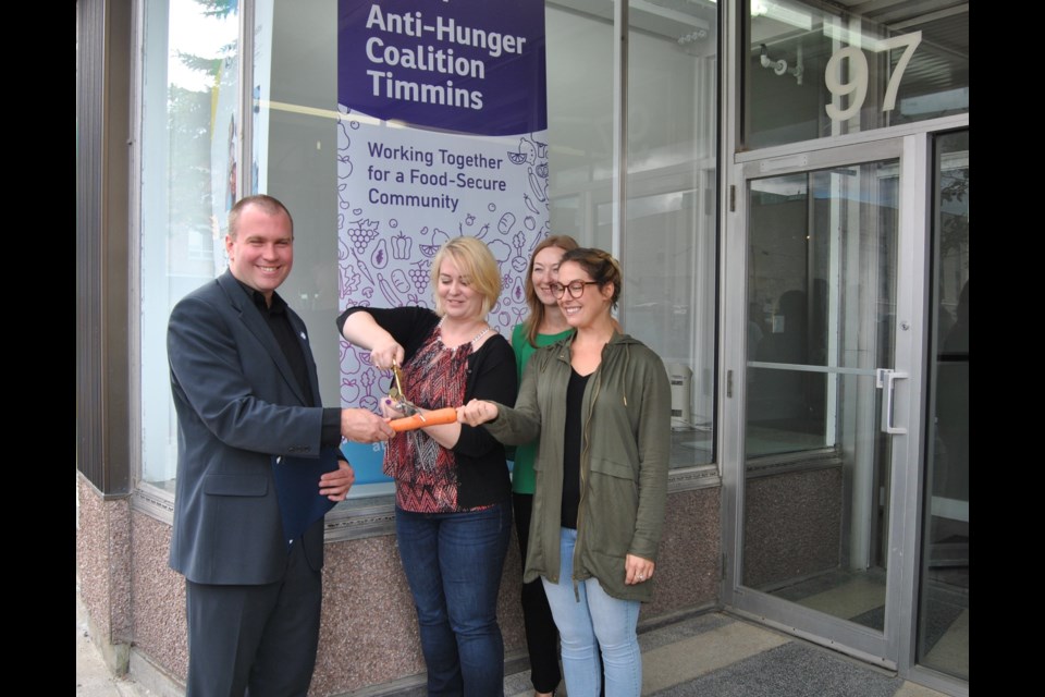 Mayor Steve Black (left) helps with the official opening of the  Anti- Hunger Coalition Timmins office on 97 Pine St. S. by holding one end of the carrot, while Michelle Goulet, ACT Executive Director wields the scissors that cut the carrot. Frank Giorno for TimminsToday. 