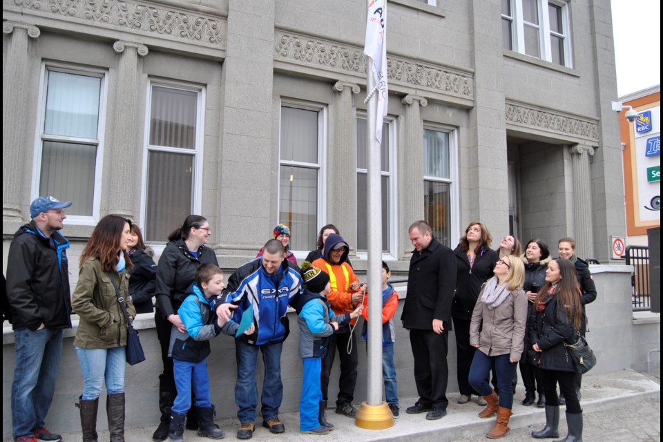 Dominque Daguerre, hidden by the flag pole, Quentin Collins to the left of the flagpole, raise the Autism Awareness Flag in front of Timmins City Hall as Mayor Steve Black, parents and representatives of NEOFACS look on in appreciation. Frank Giorno for TimminsToday.