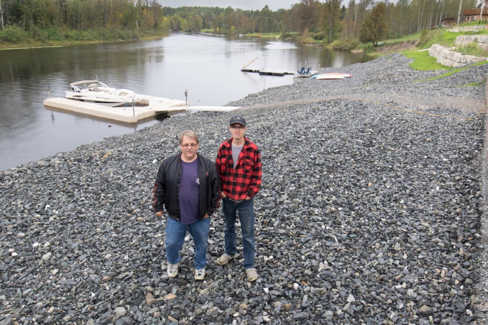 (From left) Wallingford Road residents Don Vachon and Marcel Forget stand over stones they had hauled in to prevent further degradation after large chunks of their property slipped into the Mattagami River in 2015. Before the slippage the land was grass covered and idyllic. Jeff Klassen/TimminsToday