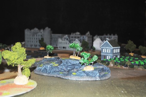 Pictured is a Flames of War game scattered with painted scenery and miniatures that simulate a WWII battle.