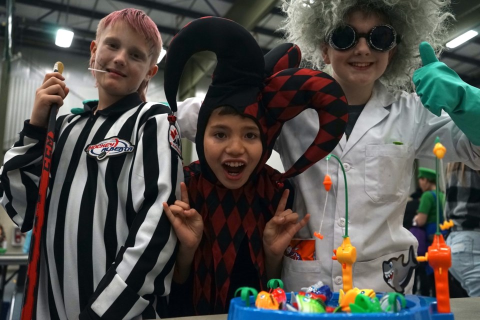 L-R, Linesman Grayson Vanboxtel, jester Farron Bernard, and mad scientist Logan Crosland pose for a photo with their sweet prizes in front of a fishing mini-game during Halloween festivities. 