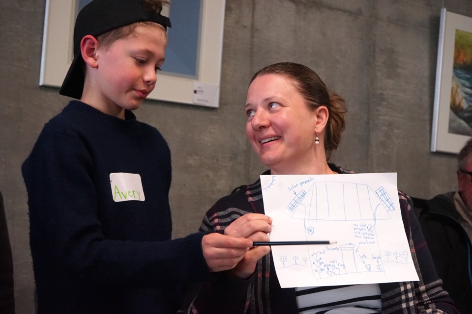 Avery Martin shows off his drawing of what elements a passive solar greenhouse could feature in Athabasca to mom Chandra Clarke, researchers, and other community members.                              