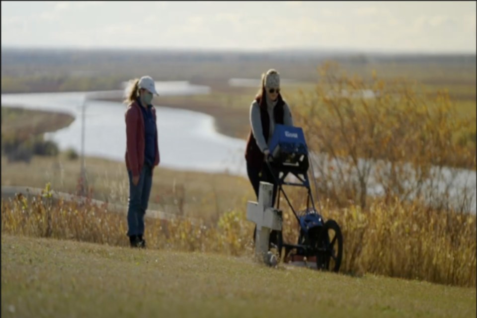 An unidentified assistant looks on as Dr. Kisha Supernant uses ground-penetrating radar to find anomalies at the Grouard Mission which may be unmarked graves of Indigenous children and adults who were forced to attend the school.