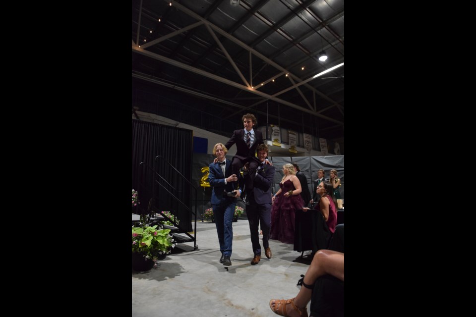 Issac Mast (left) and Reid Stephani (right) carry their classmate and fellow graduate Russell Keay around the Agrena during the grand graduate march at the banquet celebration.