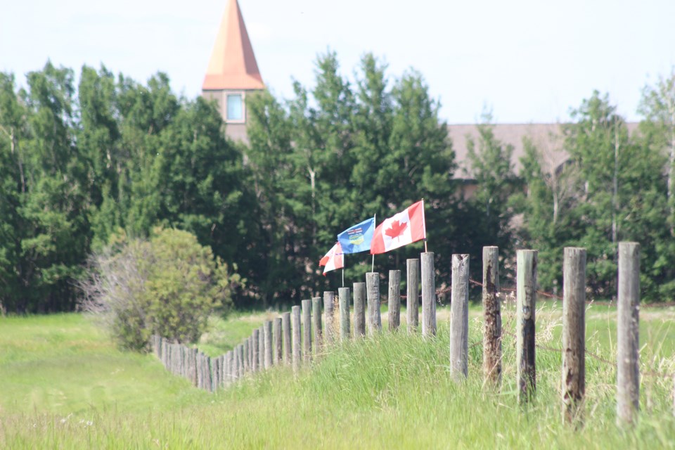 Flags wave on fenceposts in Barrhead with steeple of Canadian Reformed Church in background