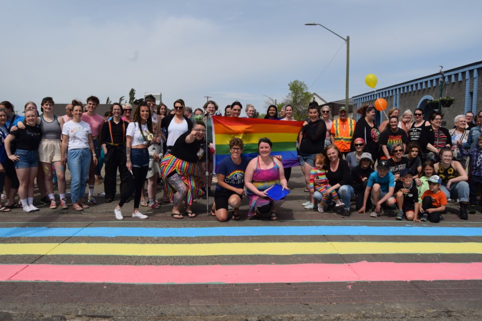 About 150 supporters on June 4 joined Cailin Clarke, an advocate for Barrhead's non-heterosexual community, to paint the first rainbow pride sidewalk on Main Street and Kowalski Drive (50 Avenue). Here Clarke (in front of the pride flag on the right) and former Barrhead native Janis Irwin, MLA for Edmonton-Highlands-Northwood (on Clarke's left.)  pose with some of the supporters in front of a half-complete crosswalk. Also in attendance were Town of Barrhead mayor Dave McKenzie and Coun. Anthony Oswald. 